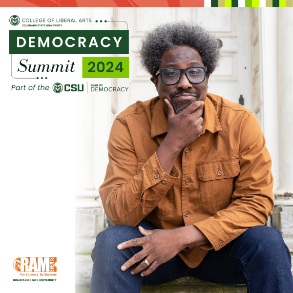 W. Kamau Bell sits with right hand on chin wearing blue jeans and an orange button down shirt.
